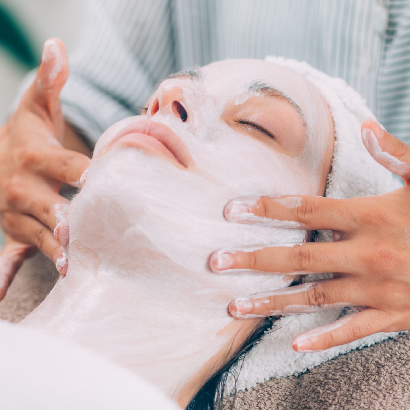 Rejuvenating Facial Mask. Cosmetologist massaging woman’s face.